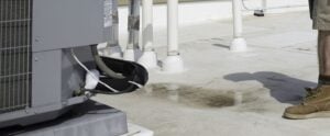 Frozen air conditioning unit mounted on commercial rooftop with white support columns and person in work boots nearby.