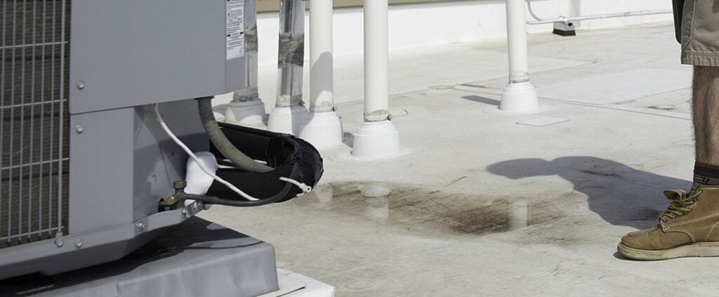Frozen air conditioning unit mounted on commercial rooftop with white support columns and person in work boots nearby.