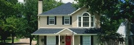 Two-story colonial house featuring blue shutters, arched window, red front door, and mature landscaping surrounding the property.