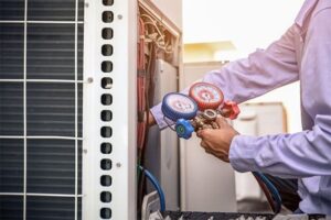 Technician in purple shirt holding red and blue refrigerant gauges while servicing air conditioning unit.