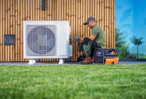 HVAC technician in green shirt and cap performing maintenance on outdoor air conditioning unit with diagnostic equipment.