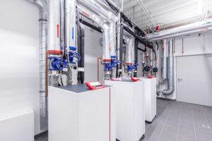 Modern commercial heat pump system with blue pumps mounted on white pedestals in a clean industrial facility with piping and controls.
